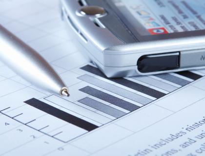 A close-up of a pen and an old phone resting on a paper with visible graphs