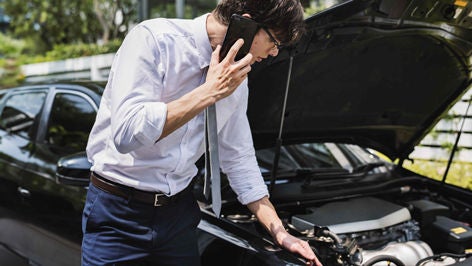 A man holding his phone to his ear while checking inside of his car hood