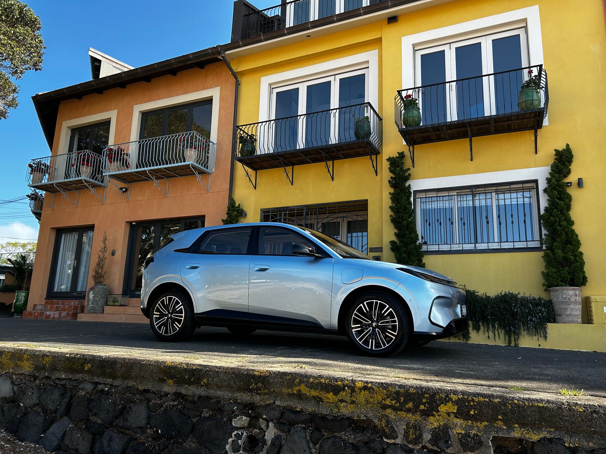 White Arcfox T1 electric SUV in side view, parked outside colourful buildings on a sunny day.