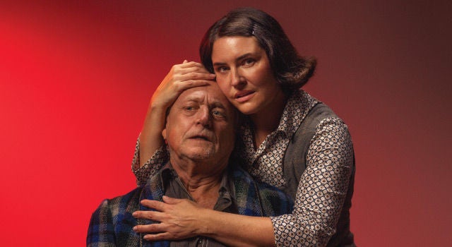 A woman holding a mans head on a read background