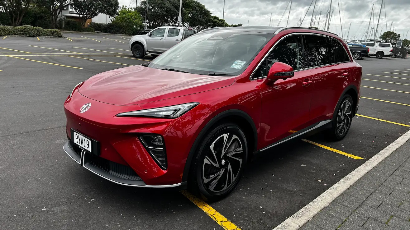 Red MG electric SUV in a car park near a marina.