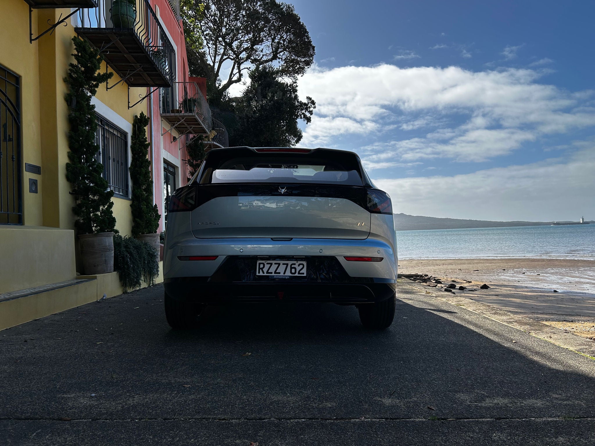 White Arcfox T1 electric SUV viewed from the rear beside a waterfront on a sunny day.