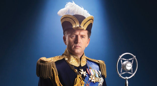 A regal man dressed in royal clothing standing in front of a microphone