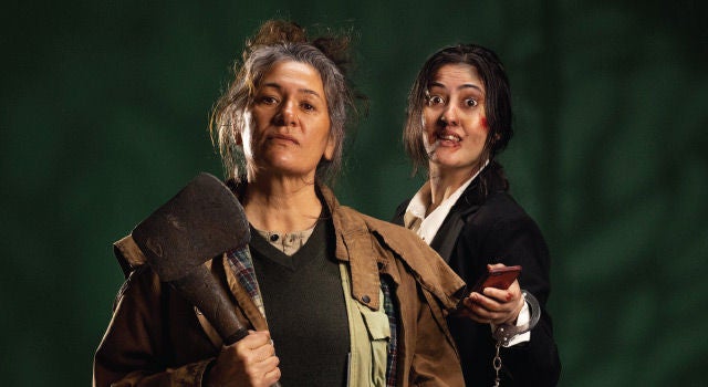Two woman standing against a moody, dark green background. One holds an axe, one is bruised and bloodied