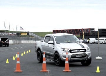 A silver ute driving around orange and yellow cones on a race car track.