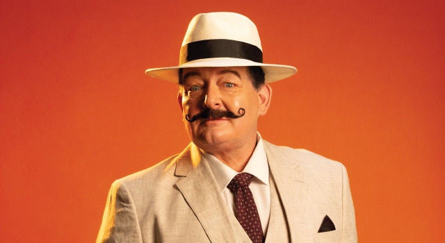 A man wearing a beige suit and white fedora with an impressive curly moustache
