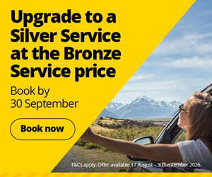 Promotional banner advertising a vehicle servicing offer. The left side of the image features a bright yellow geometric panel with bold black text reading, “Upgrade to a Silver Service at the Bronze Service price” followed by “Book by 30 September” and a yellow “Book now” button outlined in black. The right side shows a scenic outdoor photograph taken from a vehicle, with a person extending an arm out of the window toward a mountainous landscape under a blue sky. Small text along the bottom reads: “T&Cs apply. Offer available 17 August - 30 September 2026.” The overall design uses yellow, black, and blue tones to highlight the promotional offer.