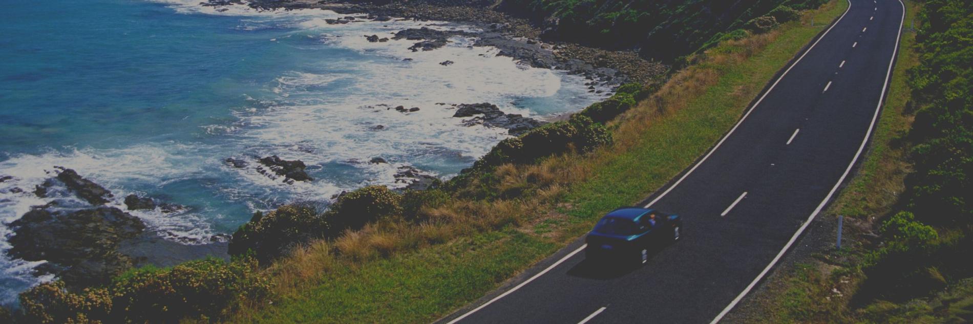 A blue car driving down the road with a beach view