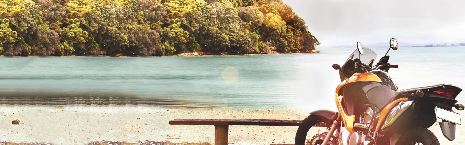 A motorcycle parked by serene beach with lush island view