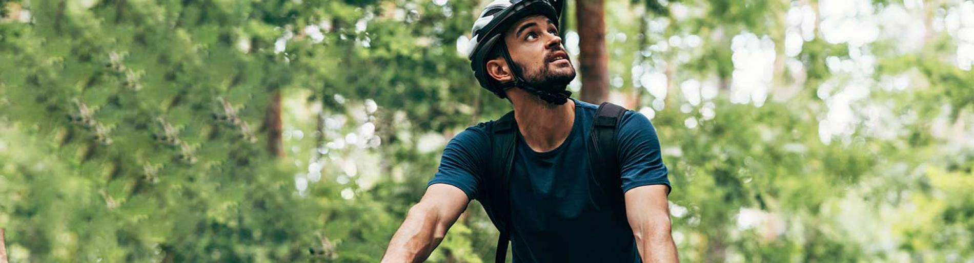 Man cycling with helmet on in a green forest