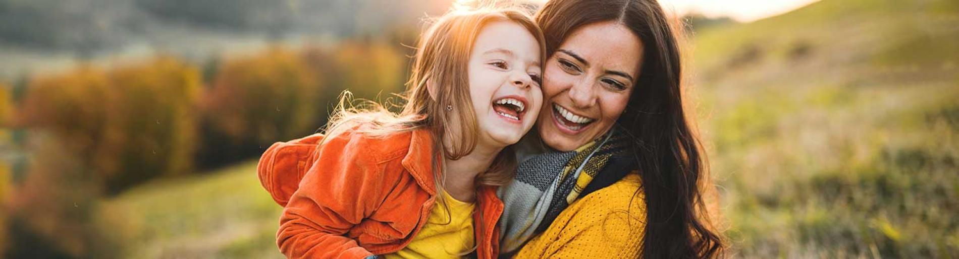 Mother and daughter laughing together outdoors in a scenic field
