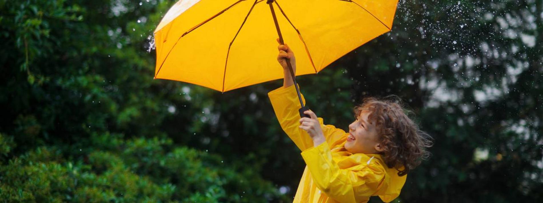 A girl dressed in a vibrant yellow rain jacket while holding a matching yellow umbrella as rain falls