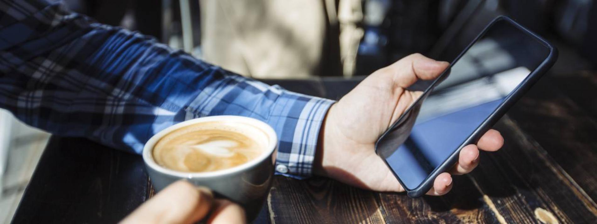 Close up image of a man holding his phone and coffee