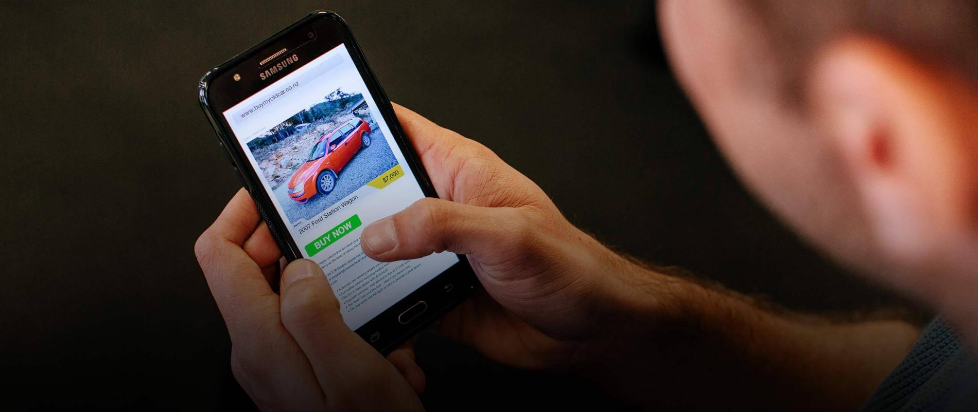 A man browsing with his phone looking to buy a red car