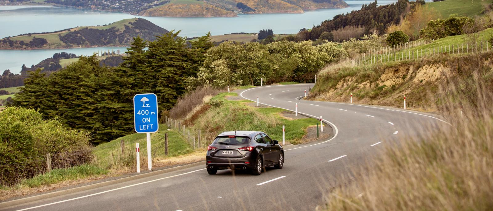 Car driving down a windy road towards Akaroa Harbour.