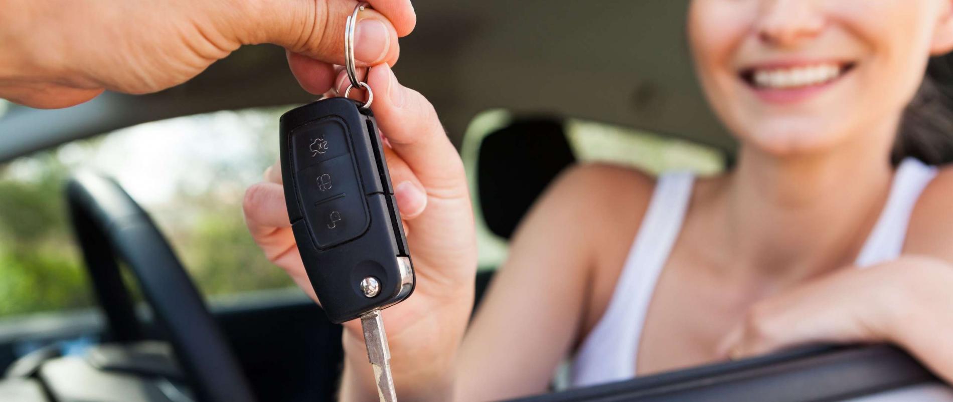 A hand giving a car key to a young driver