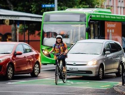 A woman riding her bike in a busy cycle lane surrounded by car and bus traffic.