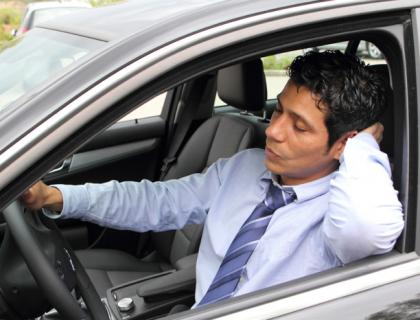A formally dressed man falling asleep in the driver's seat of his car.