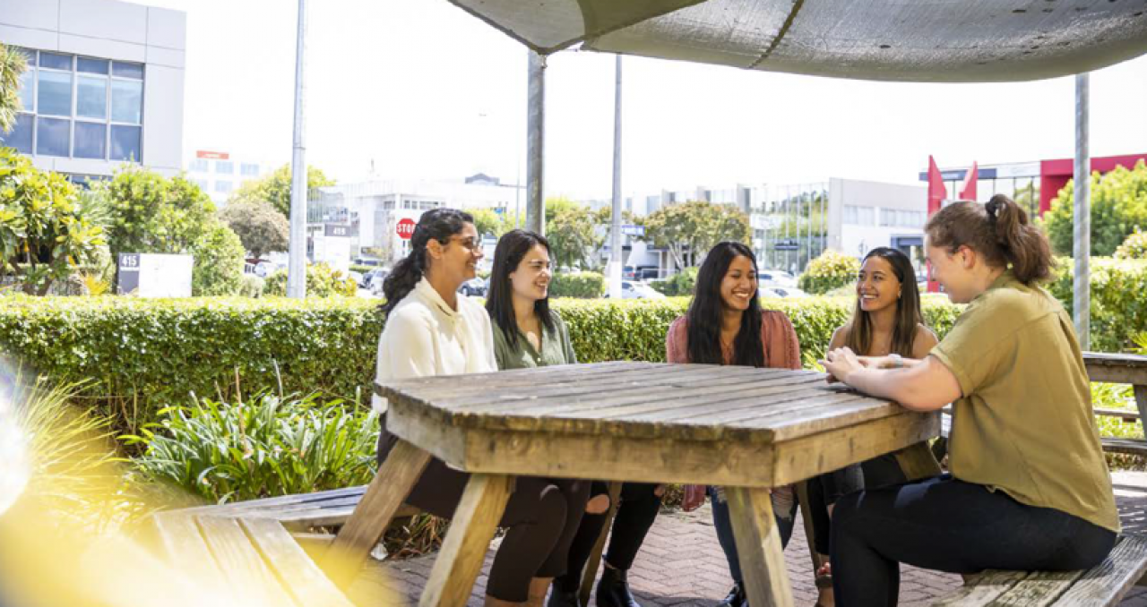 A group of women laughing while sitting on an outside table