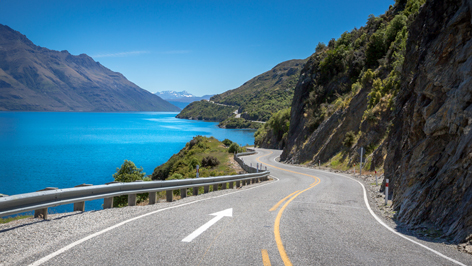 Winding coastal road beside a blue lake with mountains ahead