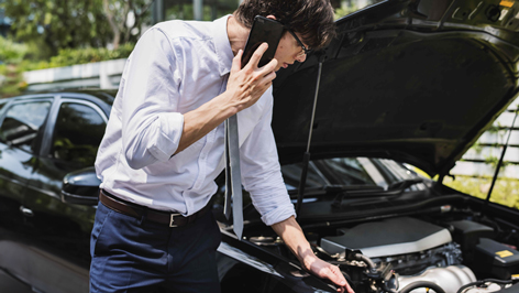 A man holding his phone to his ear while checking inside of his car hood