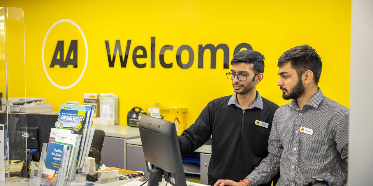 Two staff behind a help desk at an AA Driver and Vehicle Licensing Agent location.