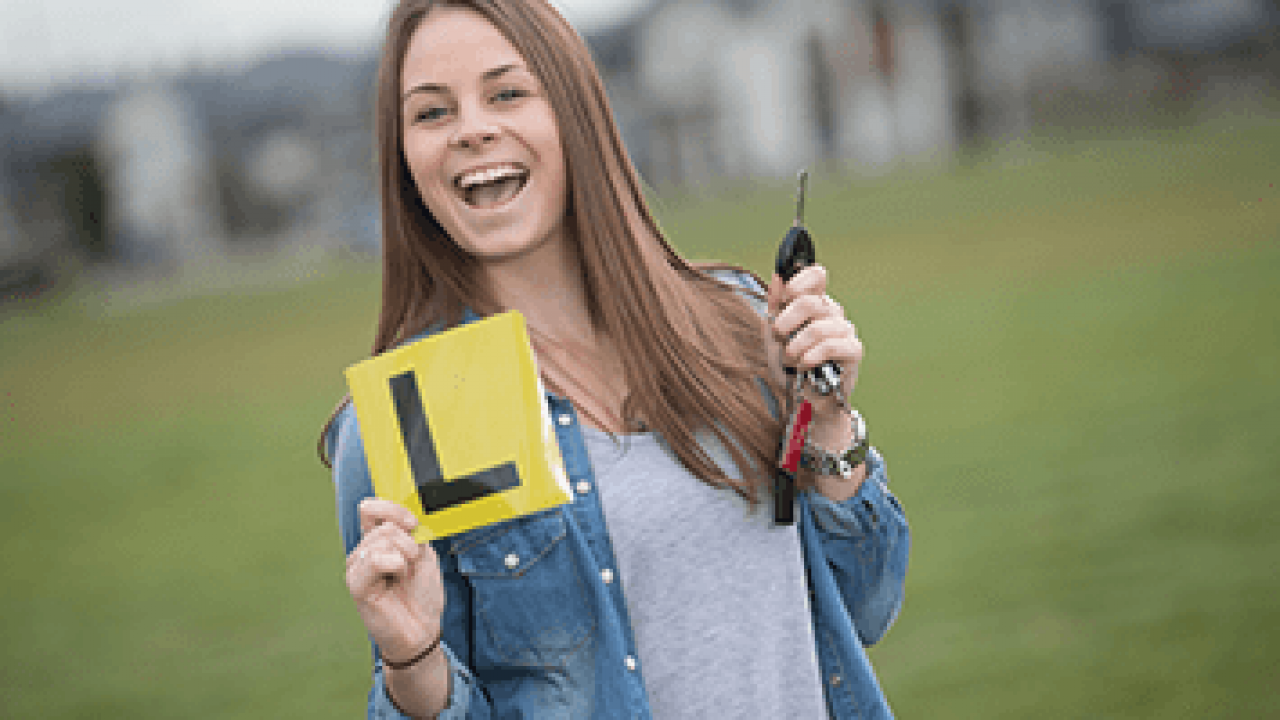 A woman smiling happily while holding an L plate and car keys