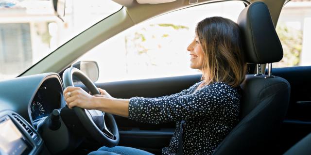 A woman smiling in the driver's seat of a car with her hands on the steering wheel