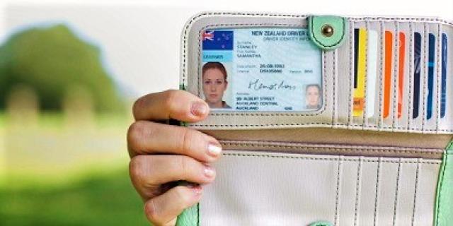 A hand holding up a wallet to display a New Zealand Drivers Licence