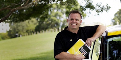 An AA Driving Instructor leaning one arm against an AA Driving School car