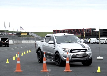 A silver ute driving around orange and yellow cones on a race car track.