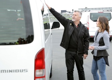 Man explaining a minibus to a woman next to him.