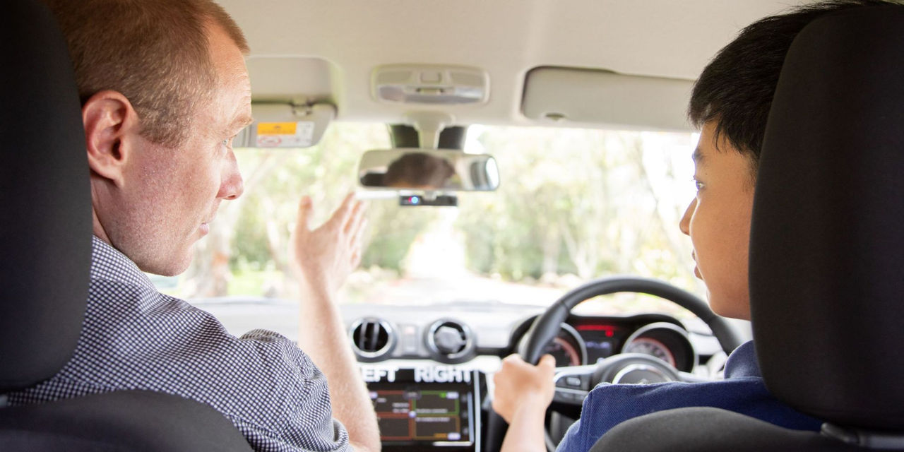 A driving instructor pointing ahead while sitting next to a student driver