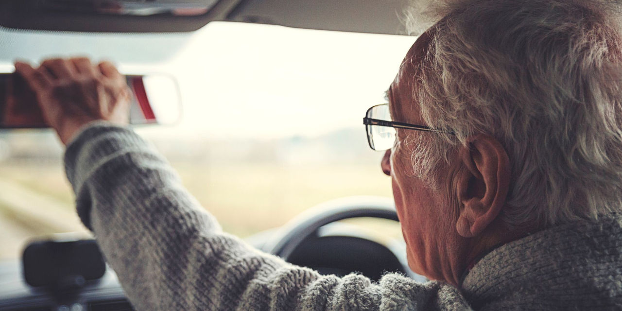 Male senior driver adjusting car mirror 