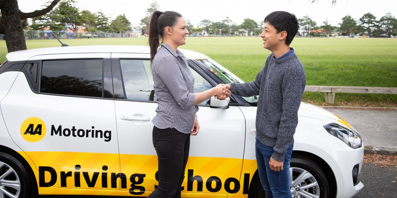 A woman driving instructor shaking hands with a student driver