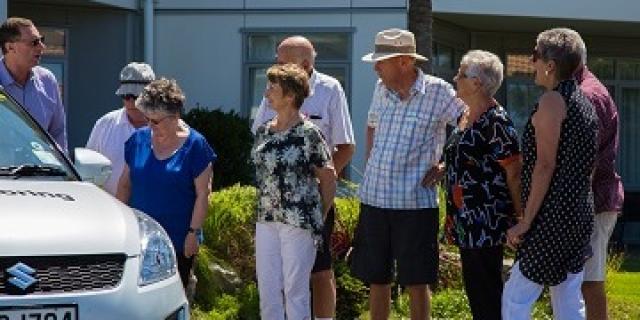 Group of elderly people standing outside a car