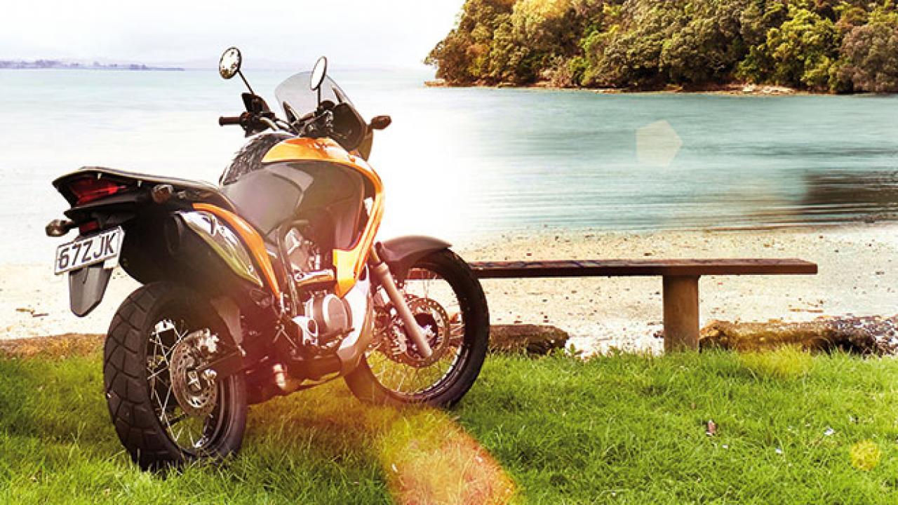 A motorcycle parked by serene beach with island view