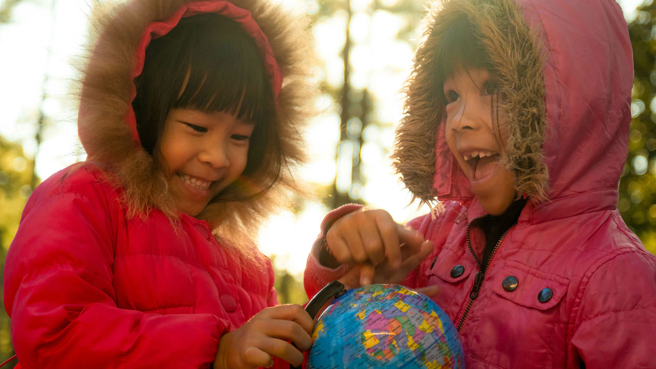 Two young girls in matching pink jackets are looking at a model globe