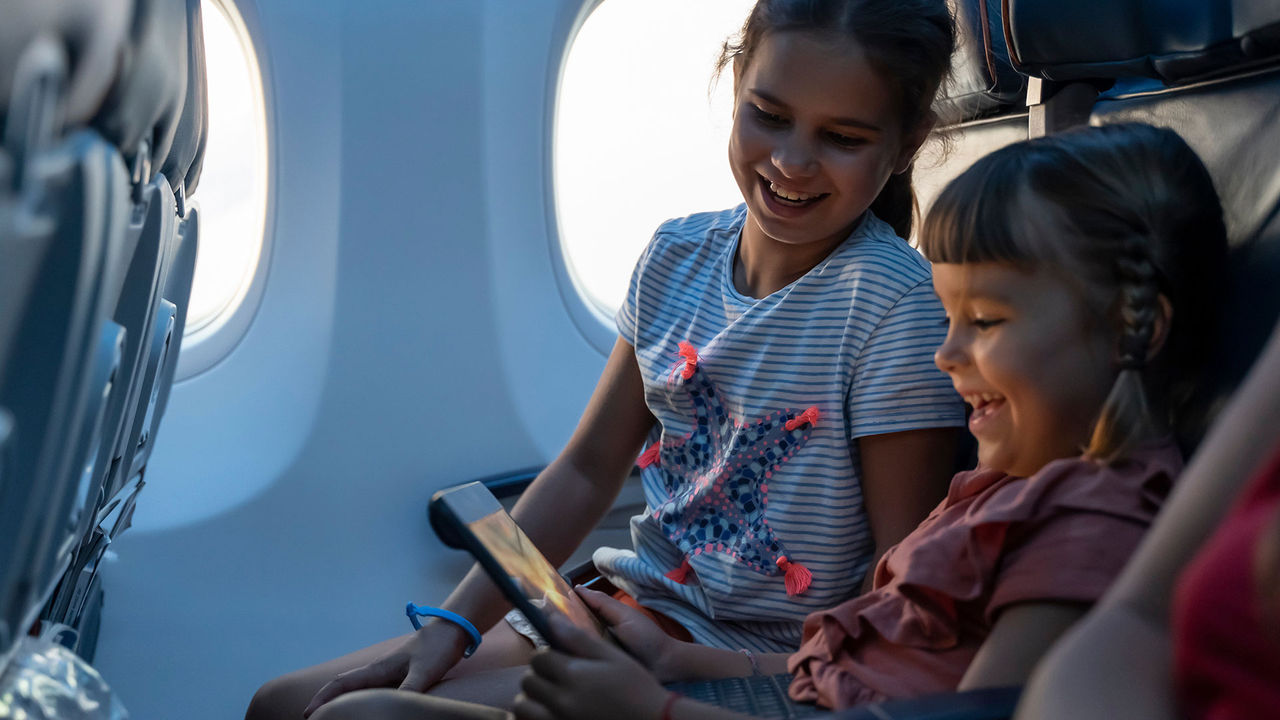 Two sisters in airplane seats smiling at an tablet screen