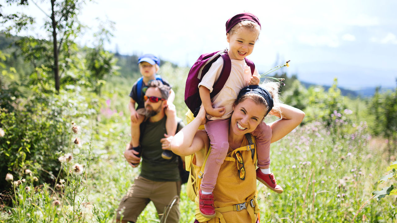 Two parents carrying their young children over their shoulders as they walk through a field