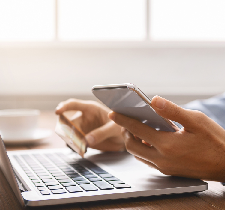 Hands rested on laptop keyboard with card and phone in hand.