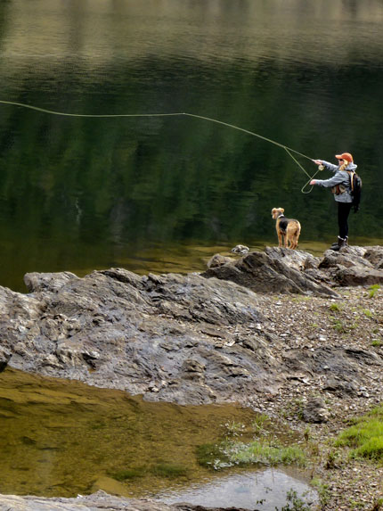 A woman fishing with her dog beside her