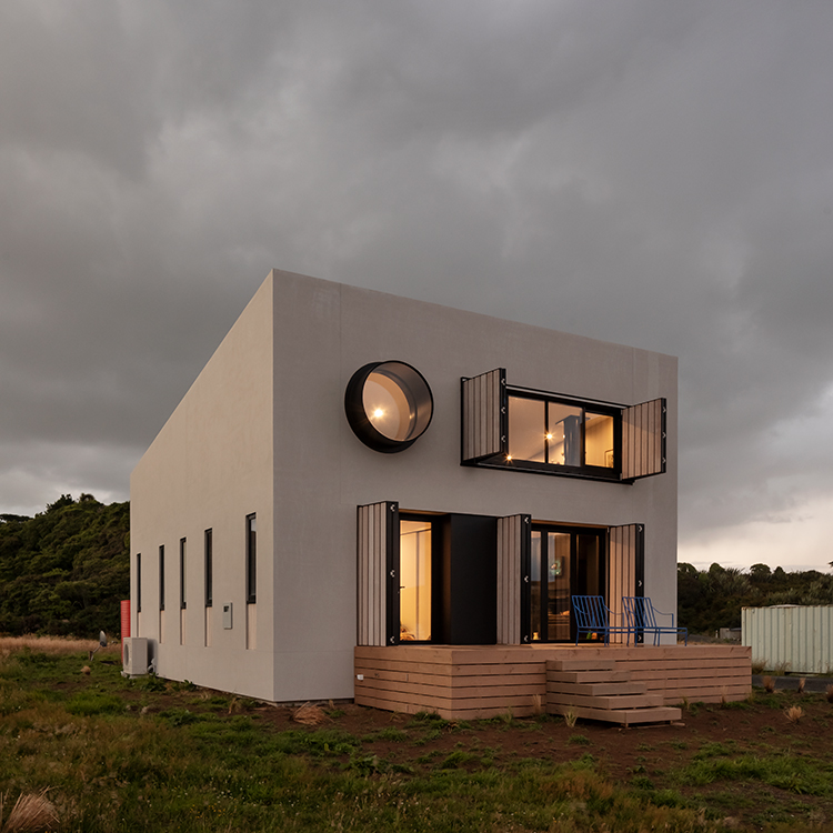 Modern boxlike holiday home with protruding feature windows and deck.