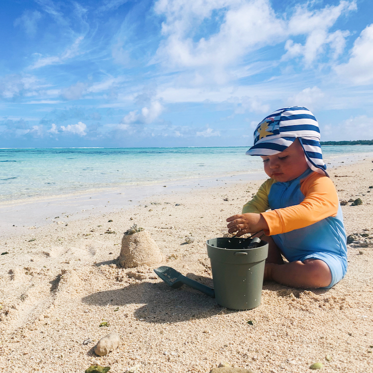 Toddler using a bucket to make sandcastles on white sand beach