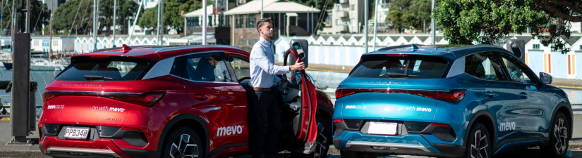 Man exiting a red Mevo branded car next to a blue Mevo branded car