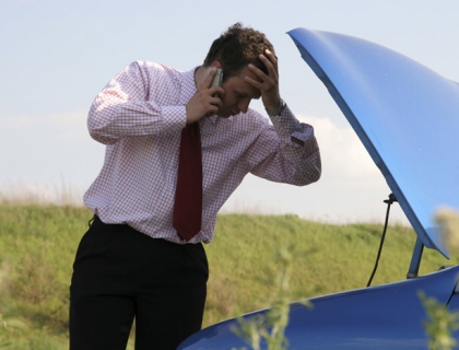 Man on phone looking concerned at his car engine
