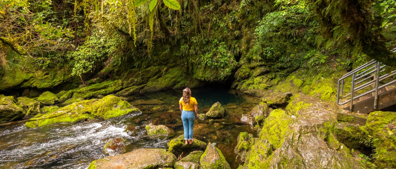Woman standing on mossy rocks in a running stream.