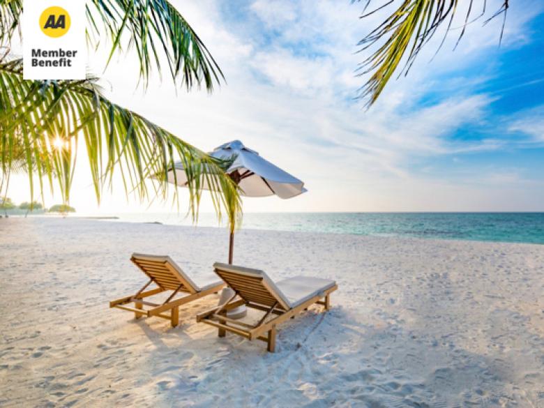 Two beach chairs with a sun umbrella are on the sand facing the shore