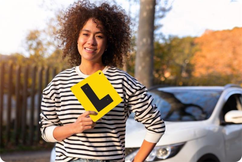 Young woman holding up an L plate for learner drivers