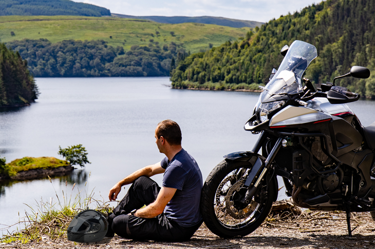 Man sitting next to a motorcyle helmet and motorbike
